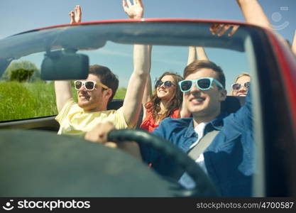 leisure, road trip, travel and people concept - happy friends driving in cabriolet car at country and waving hands