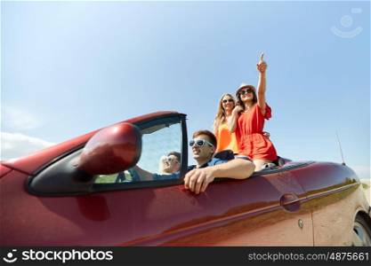 leisure, road trip, travel and people concept - happy friends driving in cabriolet car along country road and pointing finger to something