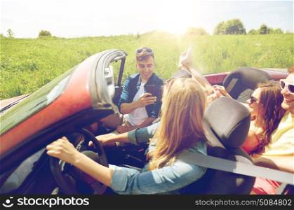 leisure, road trip, travel and people concept - happy friends driving in cabriolet car and taking picture by smartphone. friends driving in car and photographing. friends driving in car and photographing