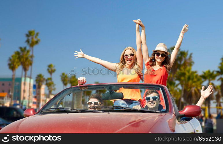 leisure, road trip, travel and people concept - happy friends driving in convertible car at country and waving hands over venice beach background in california. friends driving in car over venice beach. friends driving in car over venice beach