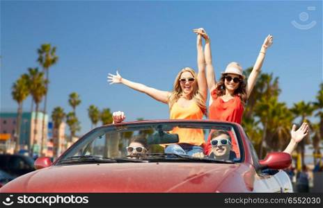 leisure, road trip, travel and people concept - happy friends driving in convertible car at country and waving hands over venice beach background in california. friends driving in car over venice beach. friends driving in car over venice beach