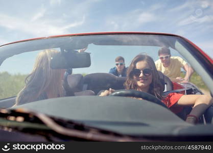 leisure, road trip, travel and people concept - happy friends pushing broken cabriolet car along country road