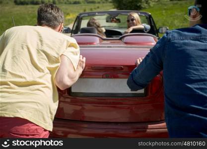 leisure, road trip, travel and people concept - happy friends pushing broken cabriolet car