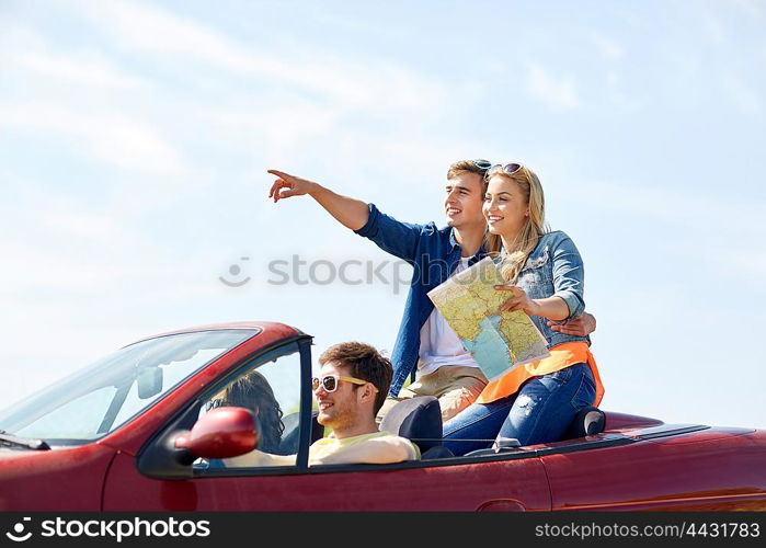 leisure, road trip, travel and people concept - happy friends with map driving in cabriolet car along country road and pointing finger to something ahead