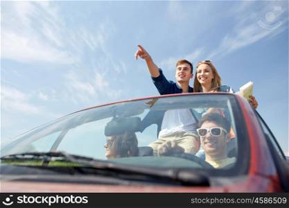 leisure, road trip, travel and people concept - happy friends with map driving in cabriolet car along country road and pointing finger to something ahead