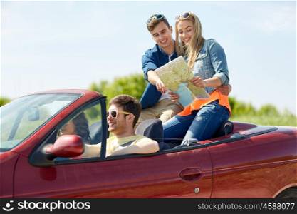 leisure, road trip, travel and people concept - happy friends with map driving in cabriolet car along country road and searching location