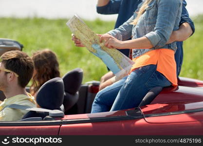 leisure, road trip, travel and people concept - happy friends with map driving in convertible car along country