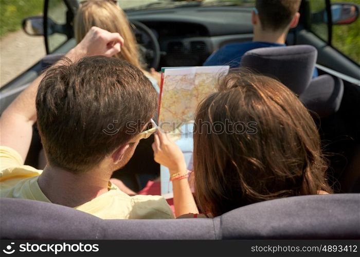 leisure, road trip, travel and people concept - happy friends with map driving in convertible car along country