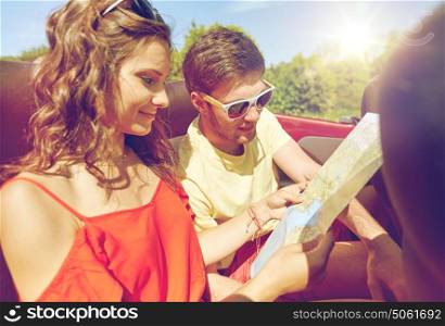 leisure, road trip, travel and people concept - happy friends with map driving in cabriolet car along country road and searching location. happy friends driving in cabriolet car
