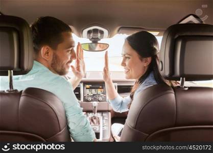 leisure, road trip, travel and people concept - happy man and woman driving in car and looking back