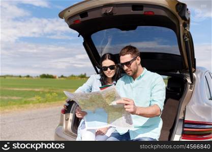 leisure, road trip, travel and people concept - happy man and woman searching location on map sitting on trunk of hatchback car outdoors