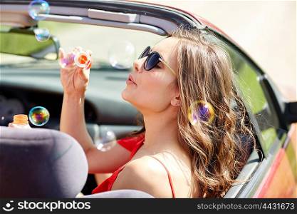 leisure, road trip, travel and people concept - happy woman blowing bubbles in convertible car