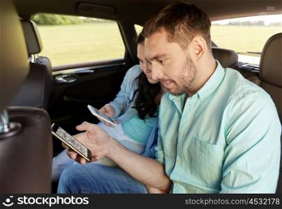 leisure, road trip, travel, technology and people concept - happy man and woman with smartphones driving in car