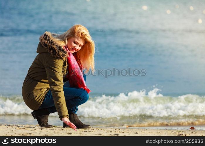 Leisure, spending free time outside, healthy walks concept. Woman wearing warm jacket relaxing on beach near sea, cold sunny day. Woman relaxing on beach, cold day