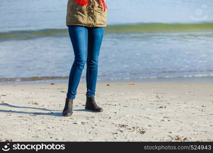 Leisure, spending free time outside, healthy walks concept. Woman wearing warm jacket relaxing on beach near sea, cold sunny day. Woman relaxing on beach, cold day