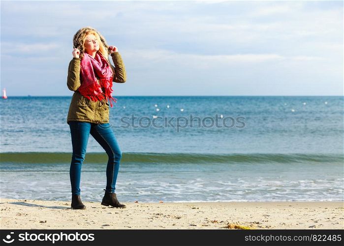 Leisure, spending free time outside, healthy walks concept. Woman wearing warm jacket relaxing on beach near sea, enjoying beautiful weather, cold sunny day. Woman relaxing on beach, cold day