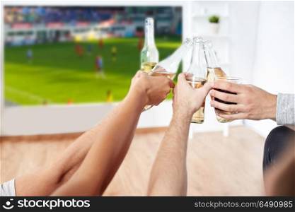 leisure, sport and people concept - happy friends clinking bottles of non-alcoholic beer and watching soccer or football on projector screen at home. friends clinking beer and watching soccer game. friends clinking beer and watching soccer game