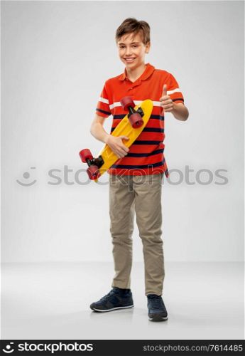leisure, sport and people concept - happy smiling boy with short skateboard over grey background. smiling boy with short skateboard