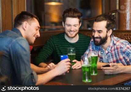 leisure, st patricks day and technology concept - happy male friends with smartphone drinking green beer at bar or pub. friends with smartphone drinking green beer at pub