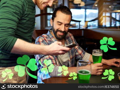 leisure, st patricks day and technology concept - happy male friends with smartphone drinking green beer at bar or pub. friends with smartphone drinking green beer at pub