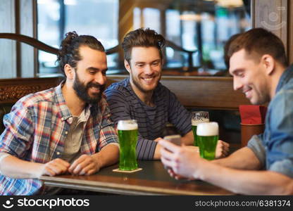 leisure, st patricks day and technology concept - happy male friends with smartphone drinking green beer at bar or pub. friends with smartphone drinking green beer at pub