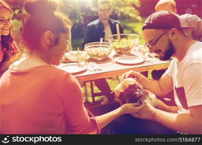 leisure, summer holidays, eating, people and food concept - happy friends with french bulldog dog having dinner at garden party. happy friends having dinner at summer garden party