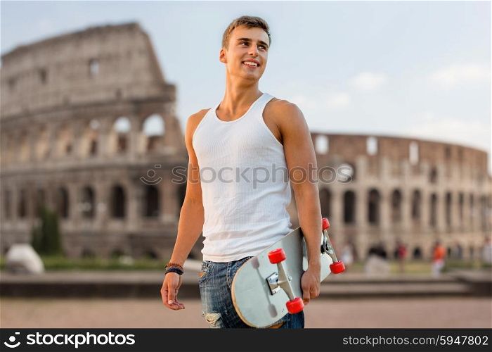 leisure, summer holidays, travel, and people concept - smiling teenage boy with skateboard outdoors over coliseum in rome background