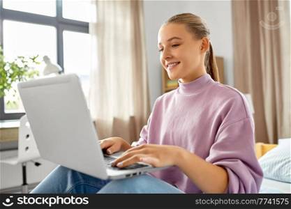 leisure, technology and education concept - happy smiling student girl with laptop computer sitting on bed at home. student girl with laptop computer learning at home