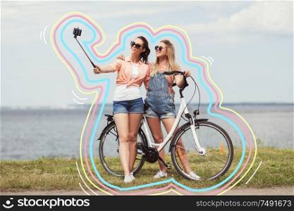 leisure, technology and friendship concept - happy smiling teenage girls or friends with bicycle taking picture by selfie stick on smartphone at seaside in summer with glowing lines. teenage girls with bicycle taking selfie in summer