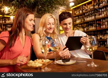 leisure, technology and lifestyle concept - happy women with tablet pc computer at wine bar or restaurant. women with tablet pc at wine bar or restaurant