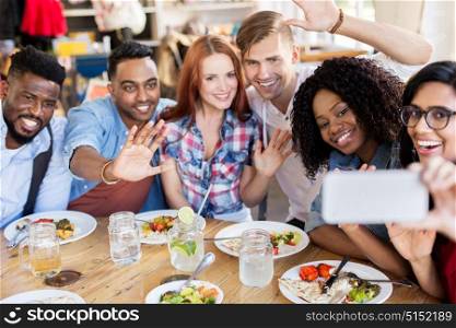 leisure, technology and people concept - group of happy international friends eating and taking selfie by smartphone at restaurant. friends eating and taking selfie at restaurant