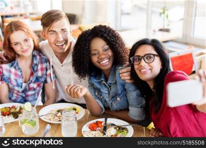 leisure, technology and people concept - group of happy international friends eating and taking picture by smartphone at restaurant. friends eating and taking selfie at restaurant