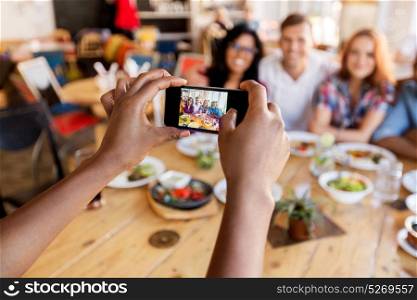 leisure, technology and people concept - group of happy international friends eating and taking picture by smartphone at restaurant table. friends taking picture by smartphone at restaurant