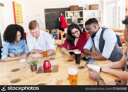 leisure, technology and people concept - group of happy international friends with smartphones and tablet pc computers drinking beer at bar. friends with smartphone, tablet pc and beer at bar