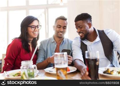 leisure, technology and people concept - group of happy international friends with smartphone at restaurant table. happy friends with smartphone at restaurant