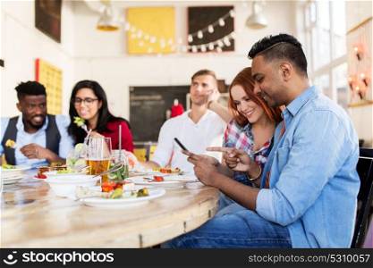 leisure, technology and people concept - group of happy international friends with smartphones at restaurant table. happy friends with smartphones at restaurant