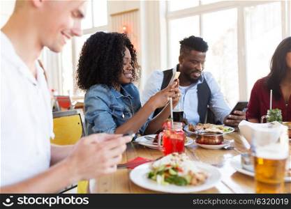leisure, technology and people concept - group of happy international friends with smartphones at restaurant table. happy friends with smartphones at restaurant