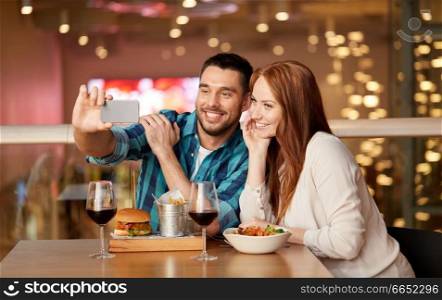 leisure, technology and people concept - happy couple having lunch and taking selfie by smartphone at restaurant. couple taking selfie by smartphone at restaurant