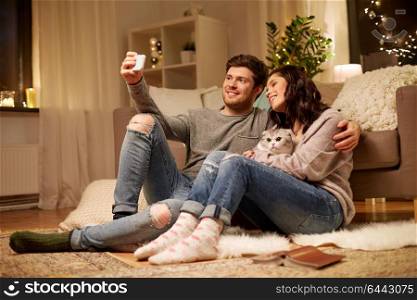 leisure, technology and people concept - happy couple with cat taking selfie by smartphone at home. happy couple taking selfie by smartphone at home
