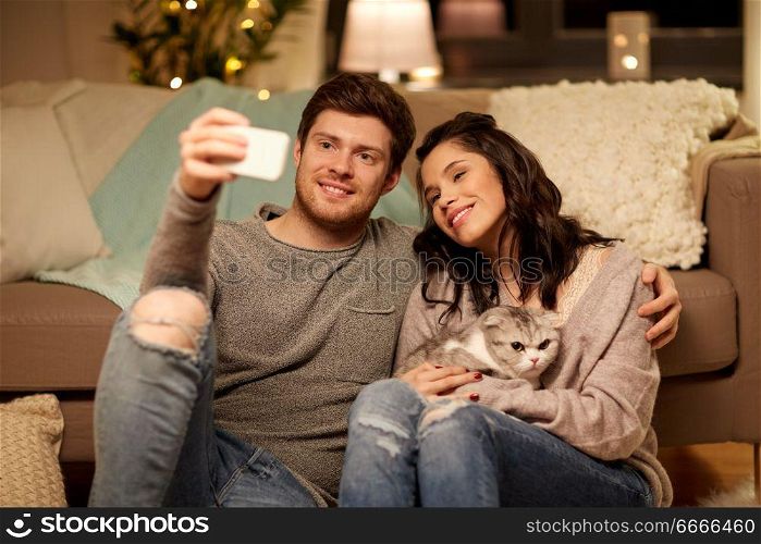 leisure, technology and people concept - happy couple with cat taking selfie by smartphone at home. happy couple taking selfie by smartphone at home. happy couple taking selfie by smartphone at home