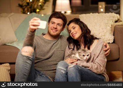 leisure, technology and people concept - happy couple with cat taking selfie by smartphone at home. happy couple taking selfie by smartphone at home. happy couple taking selfie by smartphone at home