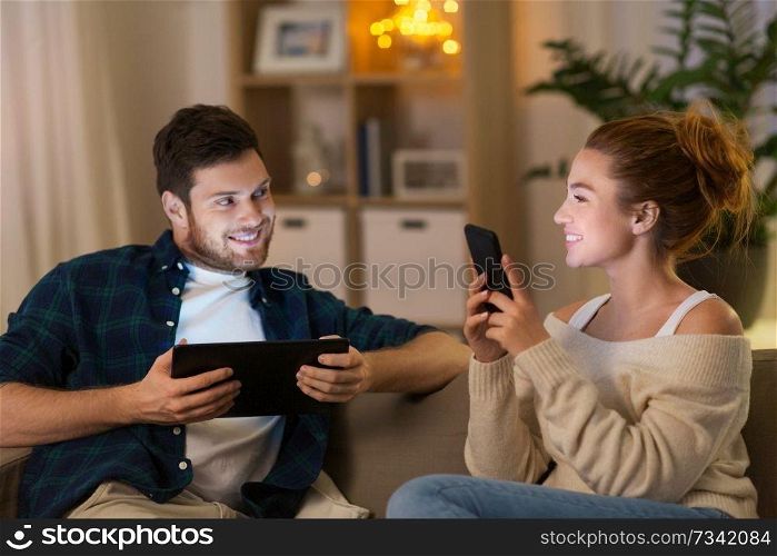 leisure, technology and people concept - happy couple with tablet computer and smartphone at home in evening. couple with tablet computer and smartphone at home