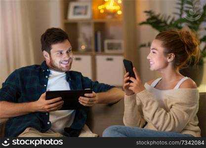 leisure, technology and people concept - happy couple with tablet computer and smartphone at home in evening. couple with tablet computer and smartphone at home