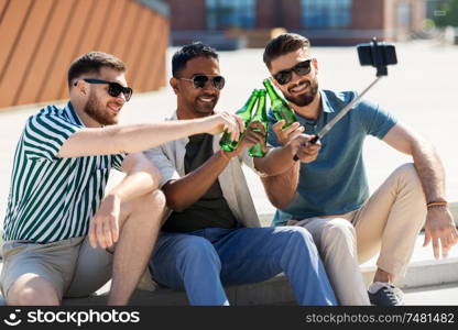 leisure, technology and people concept - happy male friends taking picture by smartphone on selfie stick and toasting beer on street in summer. men toasting beer and taking selfie by smartphone