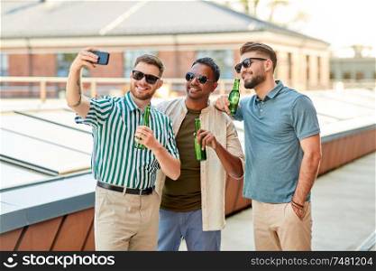 leisure, technology and people concept - happy male friends taking selfie by smartphone and drinking beer at rooftop party in summer. men drinking beer and taking selfie by smartphone