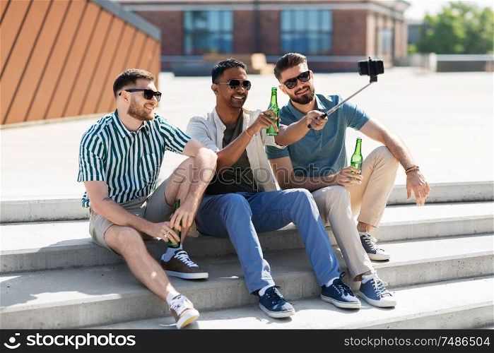 leisure, technology and people concept - happy male friends taking selfie by smartphone and toasting beer on street in summer. men toasting beer and taking selfie by smartphone