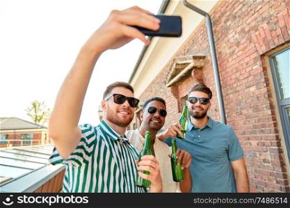 leisure, technology and people concept - happy male friends taking selfie by smartphone and drinking beer at rooftop party in summer city,. men drinking beer and taking selfie by smartphone
