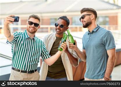 leisure, technology and people concept - happy male friends taking selfie by smartphone and drinking beer at rooftop party in summer. men drinking beer and taking selfie by smartphone