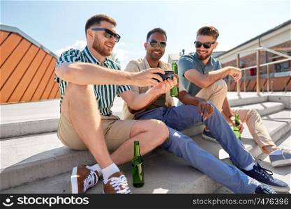 leisure, technology and people concept - happy male friends with smartphone drinking beer and talking on street in summer. men with smartphone drinking beer on street