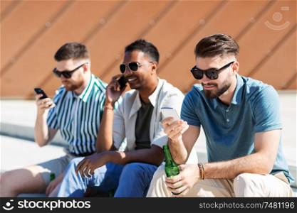 leisure, technology and people concept - happy male friends with smartphones drinking beer on street in summer. men with smartphones drinking beer on street